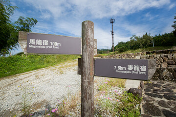 Signpost sign with directions and distance for Magome to Tsumago. Nakasendo trail Mountain valley landscape. Japanese Kiso Valley path hike, Japan. Japanese text reads 