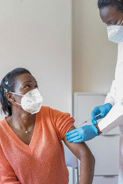 Black Woman In Mask Sitting And Getting Vaccinated Looking At Nurse