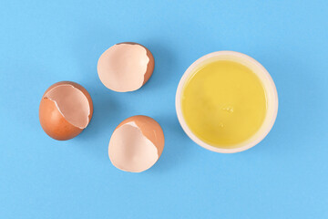 Egg white in bowl next to broken eggshells on yellow background