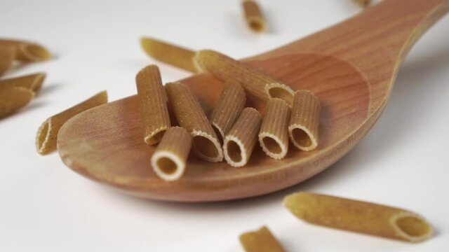 Falling dry uncooked integral pasta in slow motion into a wooden spoon on a white table. Macro shot. Organic Grain Health Food