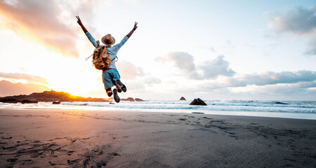 Happy man with backpack jumping over the beach at sunset - Hiker enjoying freedom outdoor on sunshine - Success, travel and people concept - obrazy, fototapety, plakaty