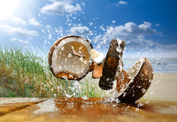 On the summer caribbean beach a fresh coconut soft drink is cracked open and the coconut juice splashes from it.