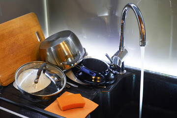 Sink with running water faucet and freshly washed dishes in the kitchen. 