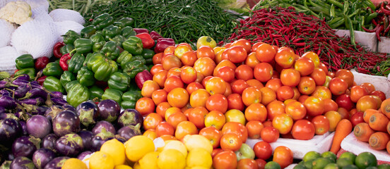 Panoramic wide angle photo of variety of fresh vegetables at market stall. Tomatoes, green peppers, aubergines, chilis and other vegetables at market stall. Select focus.