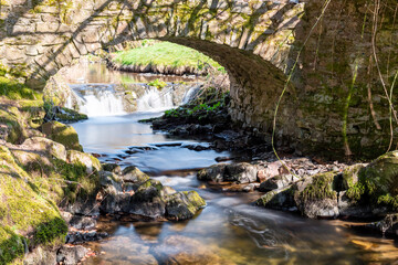 Fototapeta na wymiar Long exposure of the Weir Water river flowing under Robbers Bridge in Exmoor National Park