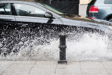 Black car crossing a road and splashing rain water at rainy weather