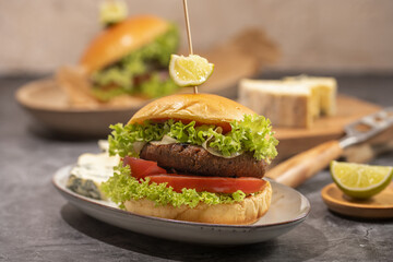 A hamburger with vegetarian patty, lettuce, tomatoes and a slice of lime on wooden board