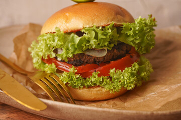 A hamburger with vegetarian patty, lettuce, tomatoes and a slice of lime on wooden board
