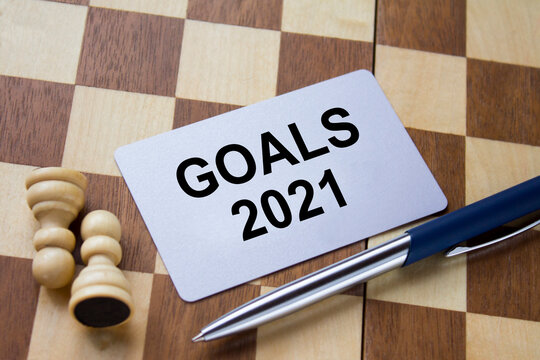 Business card with text Goals 2021 on a chess board with pen and eyeglasses