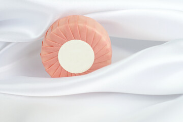 Round solid soap bar in pink paper package on white silk background