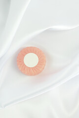 Round solid soap bar in pink paper package on white silk background