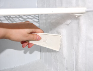 Woman cleanes the refrigerator. Woman's hand with ice scraper. Defrosting of freezer.