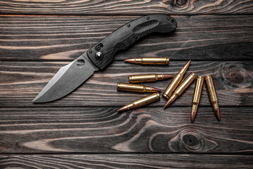 Pocket folding knife and a few rifle cartridges on a wooden back