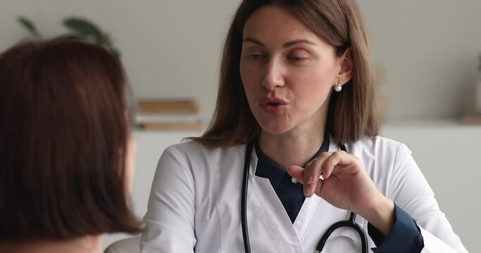 Close up female therapist in white coat talking to elderly 50s woman patient provide helpful information, give health advice telling prescriptions. Professional medicare, reliable GP doctor concept