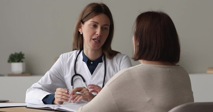 Friendly positive conversation between young female doctor in white coat and older woman patient during visit in clinic. Reliable therapist, medicare of old citizens, general health check up concept
