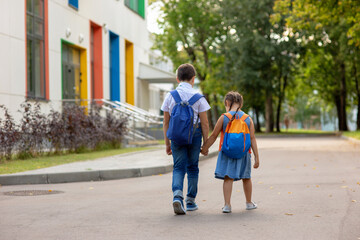 two schoolchildren, a little girl and a boy in a with backpacks go on the way to school.