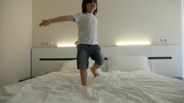 baby boy in shorts and a white T shirt jumps on the bed