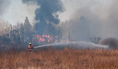 A fireman spraying water on a grass fire.