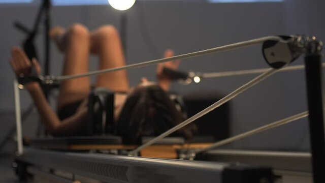 Young fit athletic woman exercising on pilates reformer machine with moving platform on tension springs.