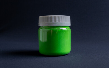 A pot containing resin of a green glitter color on a dark black background. Used for various purposes in industry and at home in the adaptation of furniture and objects for interior decoration.
