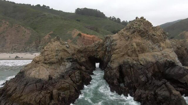 Aerial Tilt Down Shot Of Waves Splashing On Keyhole Arch, Drone Flying Forward Towards People At Famous Pfeiffer Beach - Big Sur, California