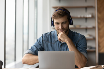 Smiling young male student in headphones watch webinar on computer study online from home. Happy man in earphones learn work distant on laptop, talk on webcam zoom video call. Education concept.