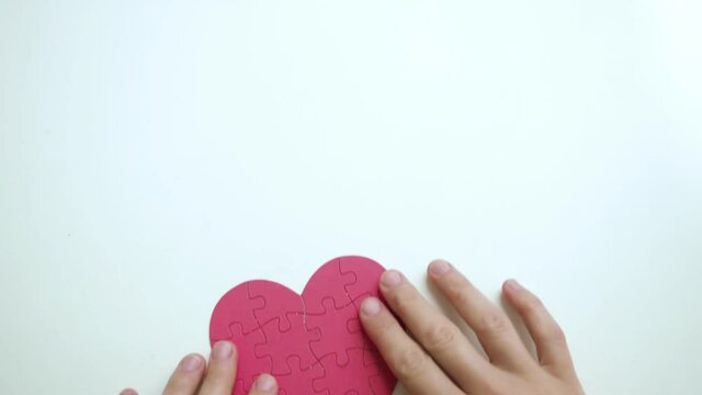 Top view on woman's hands are taken red heart shaped jigsaw from paper blocks puzzle from white table background