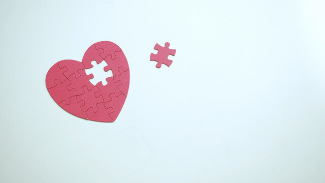 Copy spase. One piece of missing part from red puzzle heart shaped jigsaw on white table background. Top view