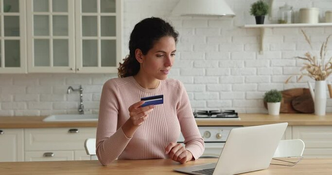 Young woman sit in kitchen use laptop holding credit card buying on-line. Satisfied client of financial operations e-payment easy electronic payment for goods, services on internet, secure pay concept