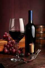 glass of red wine with bottle, background grapes and wooden barrel with wooden bottle opener and...