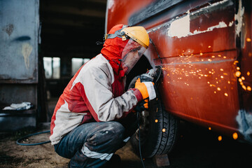man in safety helmet grinds welded seams of car body, truck body repair