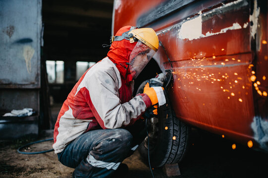 Man In Safety Helmet Grinds Welded Seams Of Car Body, Truck Body Repair