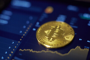 The gold bitcoin coin lies on the tablet screen, which shows cha