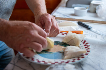 A female chef uses two hands to fold samosa pastry into small squares. There's a knife on the counter in the background. The plate that the chef is using is colorful. 