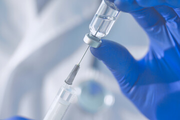 A doctor in blue gloves draws a vaccine into a syringe. Close-up.