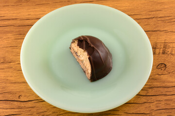 Half eaten chocolate covered dome shaped candy with sugar cookie biscuit, cappuccino jelly and whipped cream on green dessert plate