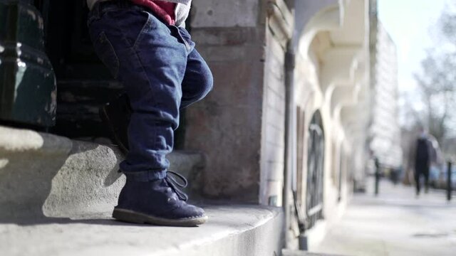 Happy child stepping outside at city street. Young toddler boy jumping