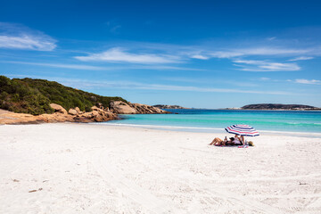 Fototapeta na wymiar Holiday makers relax under an umbrella on the pristine white sand beach and sparkling waters of Wharton Bay in the Cape LeGrande National Park