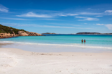 Fototapeta na wymiar A young couple swim in the sparkling water next to the pristine white sand beach of Wharton Bay in the Cape LeGrande National Park on a clear summer day.