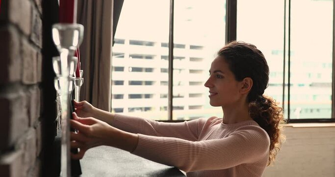 Hispanic young smiling woman keep cozy atmosphere at home, put picture in frame on surface of fireplace fix modern candlestick. Creative work of decorator, create good feng-shui in living room concept