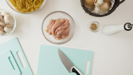 Raw pasta, chopped chicken fillet, mushrooms, onion and garlic. Ingredients close up on white background, view from above
