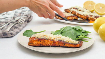Woman serving smoked paprika roasted salmon, spinach and lemon on a plate.
