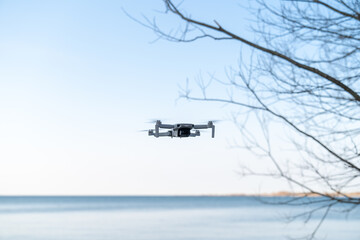 A small drone hovers above the shore of a lake