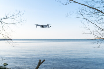 A small drone hovers above the shore of a lake