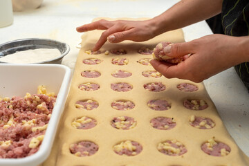 hands filling homemade pasta in sorrentino mold with ham and cheese and pumpkin filling on worktop with flour bowls and rolling pin and plastic molds