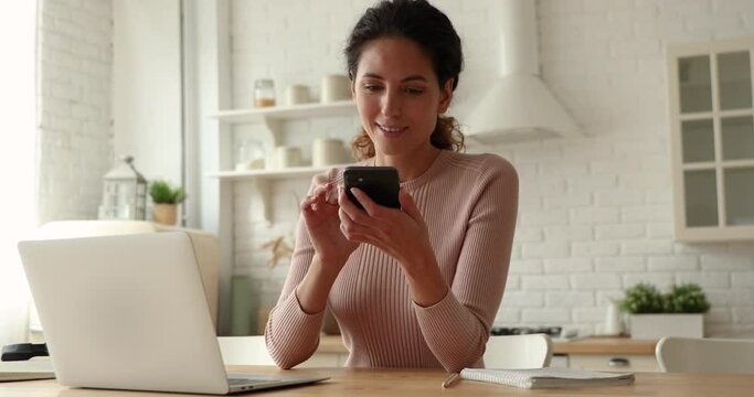 Young woman answers a call while surfing internet texting on laptop working distantly in kitchen. Telesales selling of goods or services to client over the telephone, solve business remotely concept