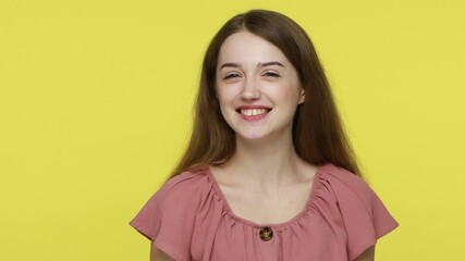 Lovely coquettish brown haired woman winking playfully, looking at camera with smile, flirting and blinking eye, cheering up with happy look. Indoor studio shot isolated on yellow background.