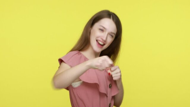 Brave beautiful brown haired female in elegant dress punching fists to camera, boxing with positive facial face expression, self defense concept. Indoor studio shot isolated on yellow background.