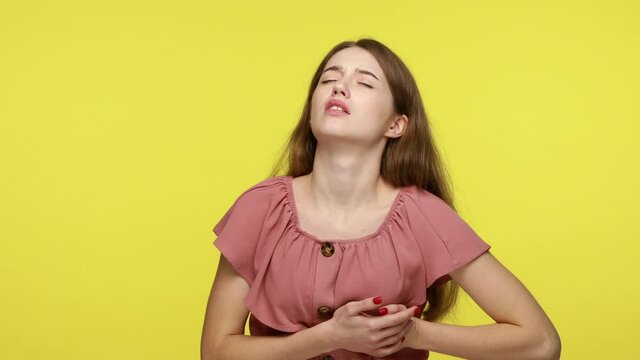 Heart attack from anxiety. Stressed young woman with brown hair clutching chest, needs emergency of acute myocardial infarction, feeling pain. Indoor studio shot isolated on yellow background.
