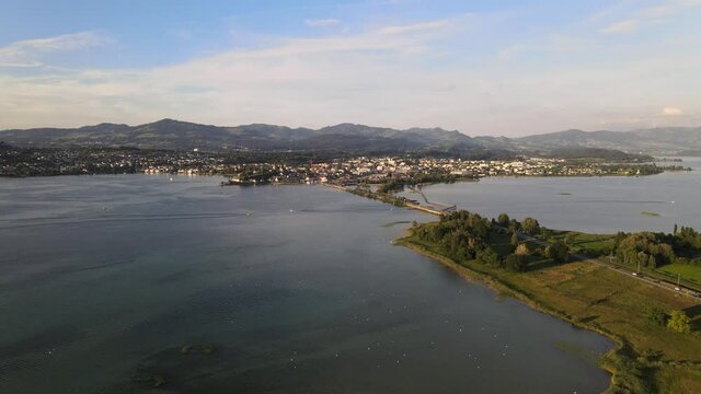 Cinematic aerial drone shot flying over lake Zurich towards Rapperswil at sunset in summer